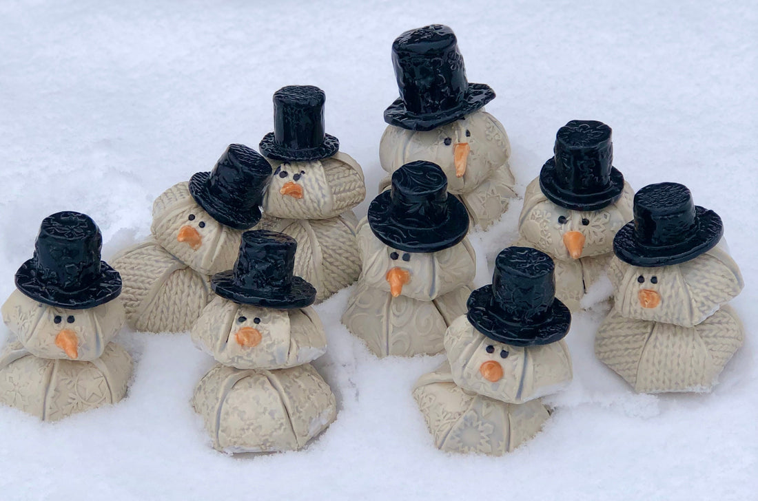 Handcrafted ceramic snowmen displayed in fresh snow, featuring textured details and festive charm from ChickaBee Pottery’s holiday collection