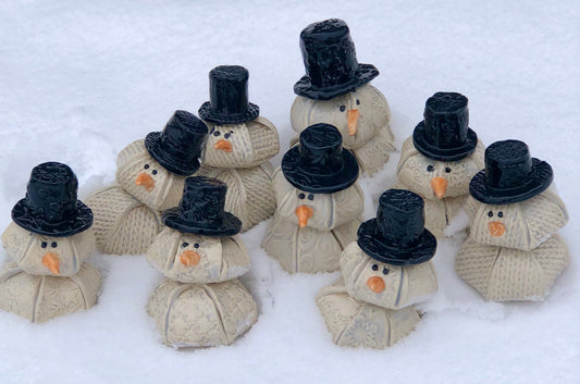 Handcrafted ceramic snowmen displayed in fresh snow, featuring textured details and festive charm from ChickaBee Pottery’s holiday collection